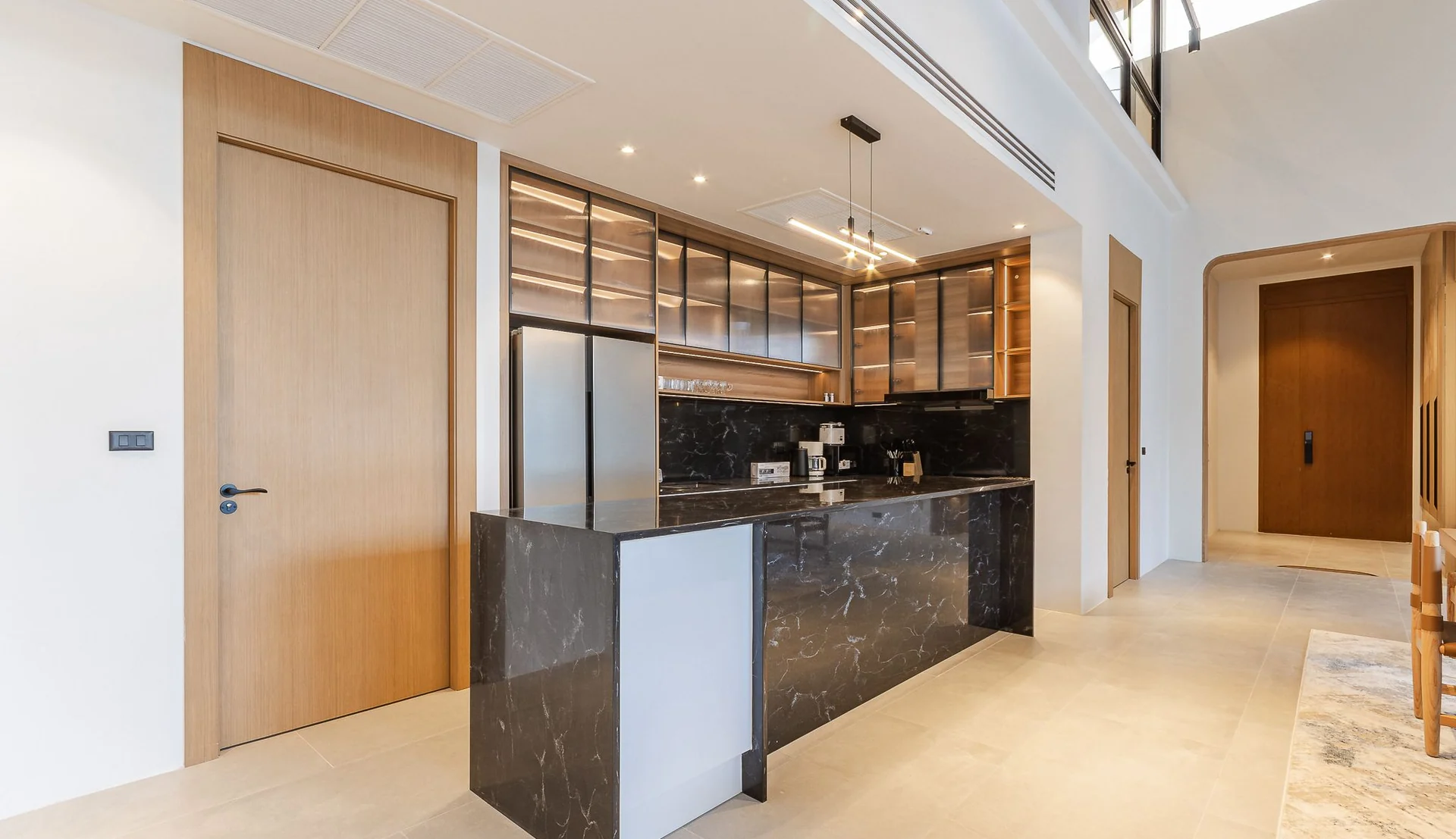 Villa kitchen with a black marble island, wood-grain tall units and glass-front upper cabinets in a bright open-plan interior