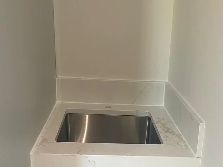 Undermount stainless basin set into a stone-look counter with matching backsplash in a new utility cabinet