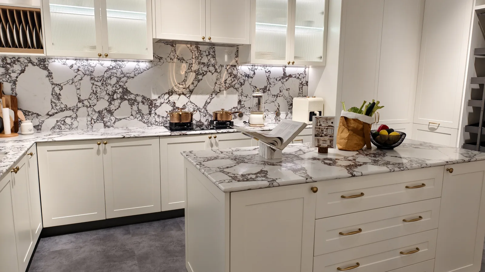 White kitchen with gold bar pulls, reeded glass uppers and a marble-look worktop