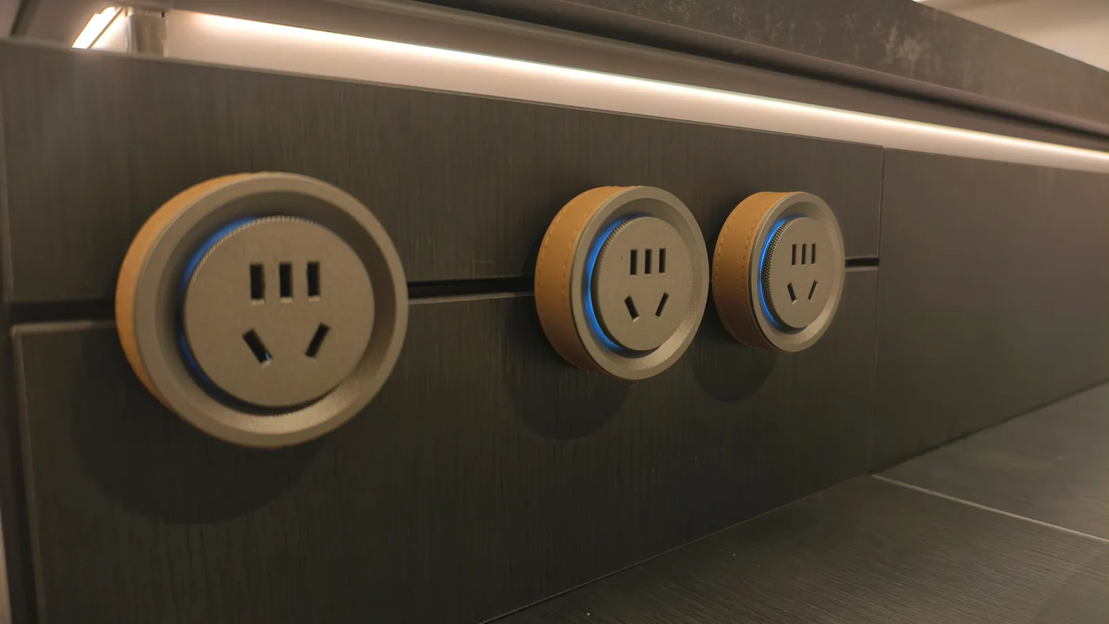 Dark wood-grain panel with three gold-and-black round sockets under an integrated light line