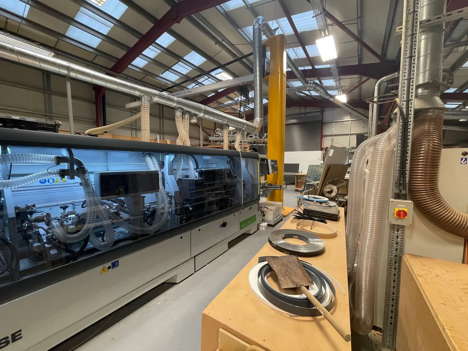A large edge-banding line running inside a cabinet factory, seen down the length of the machine