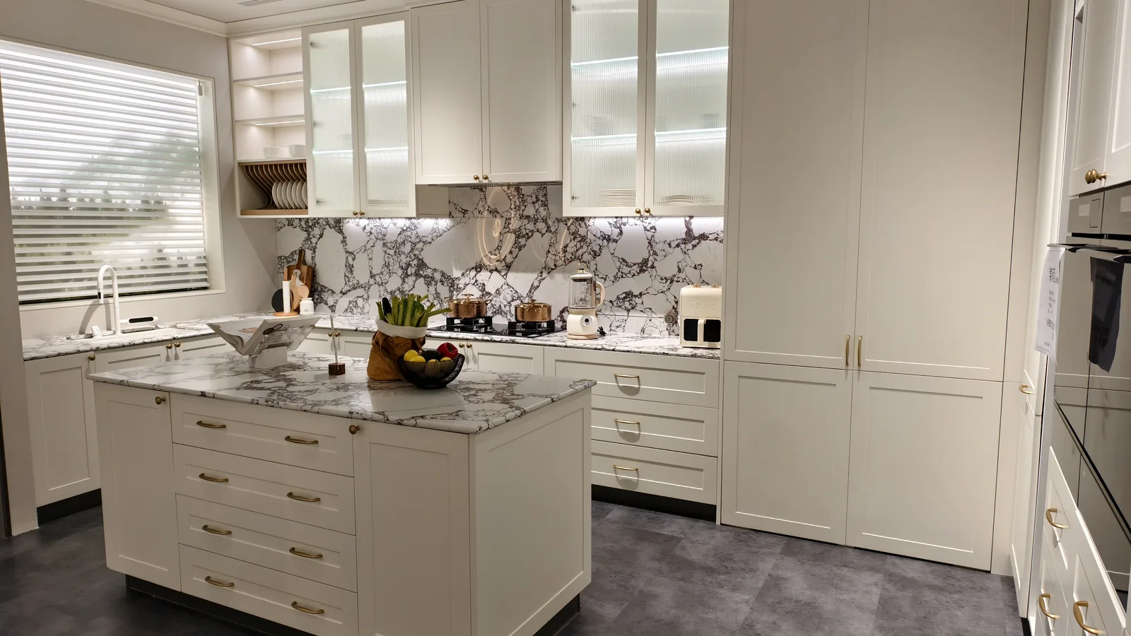 A completed white kitchen with marble splashback, island and tall units, installed on a villa project