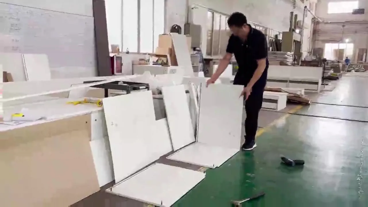 Installer handling cabinet panels on the assembly bench with the drawing sheet posted on the wall behind him