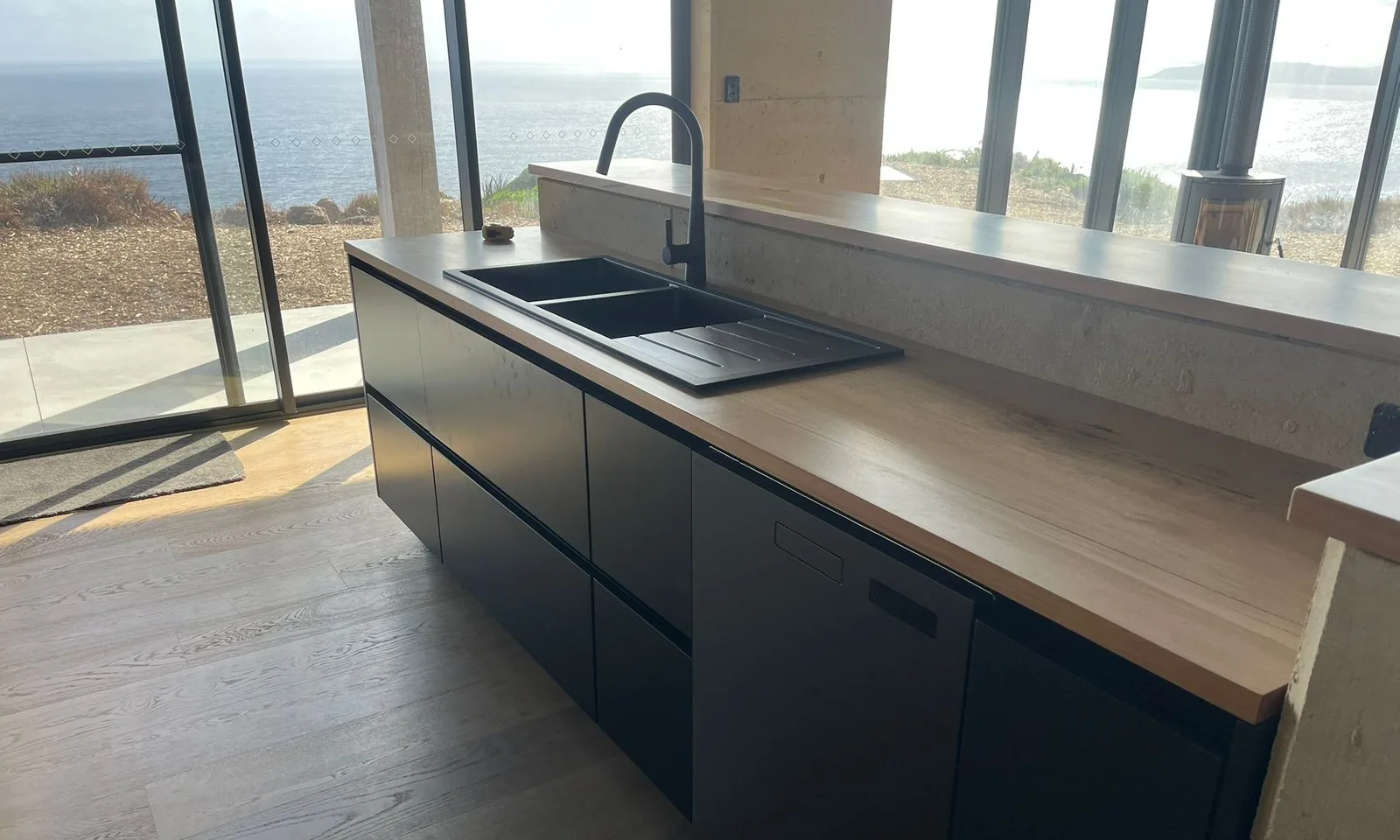 UK house kitchen with dark base units and a pale stone worktop facing full-height windows
