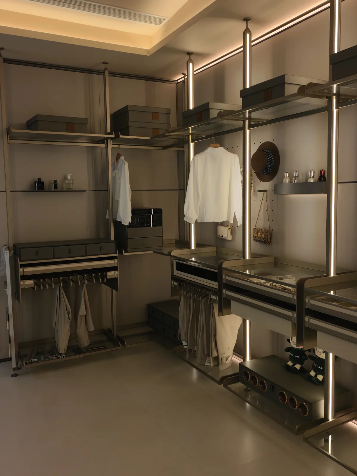 Open wardrobe system in our partner's showroom with LED strips glowing inside the uprights either side of the hanging bays, plus a ceiling cove wash above