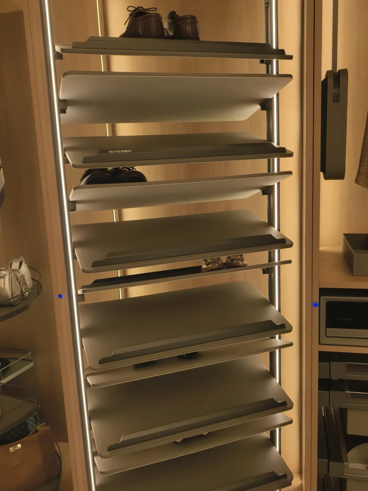 Rotating shoe tower in a wardrobe column with light grey tilted shelves, LED strips on both uprights and one pair of dark shoes on the top shelf