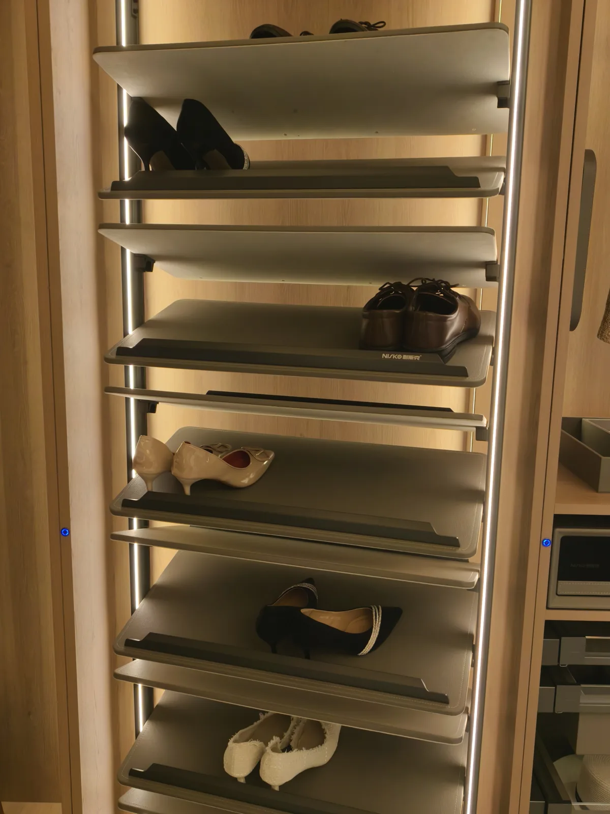 Rotating shoe tower with mixed footwear on tilted shelves - heels, flats and lace-up shoes - lit by LED strips along the uprights