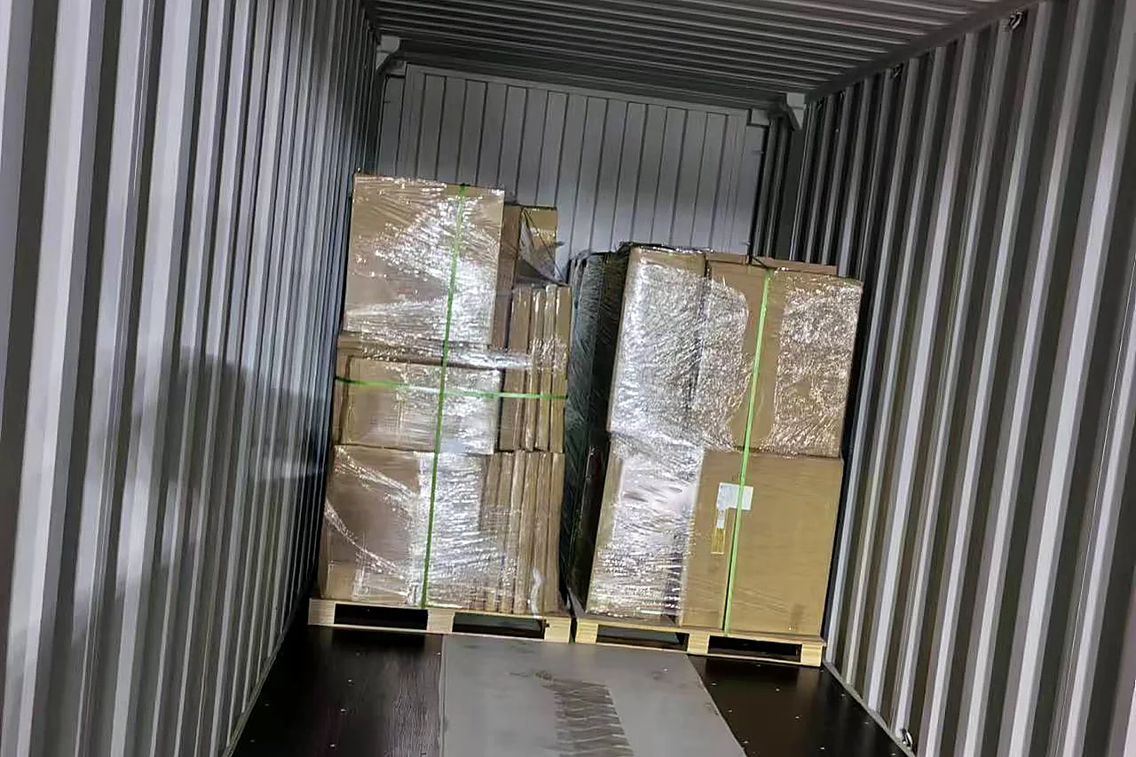 Wrapped and strapped cabinet pallets racked inside an ocean container, doors open at the factory