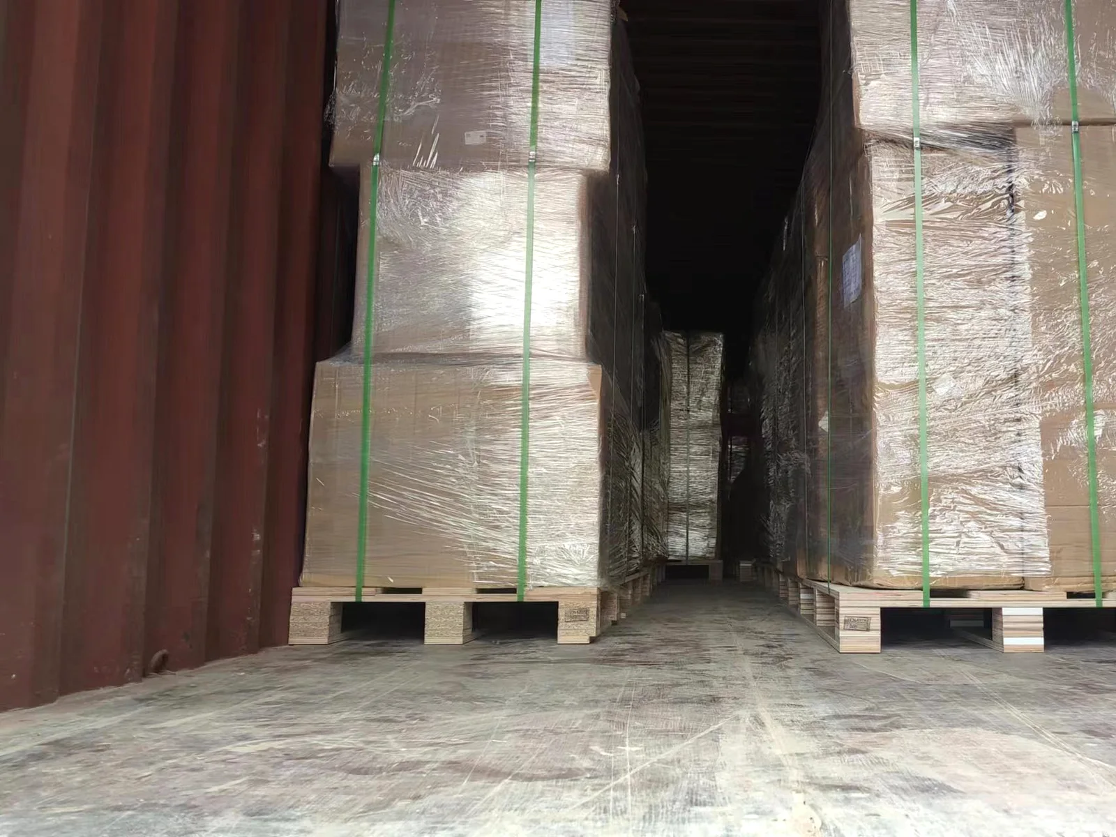 Shrink-wrapped flat-pack cabinet loads strapped on pallets inside the export container