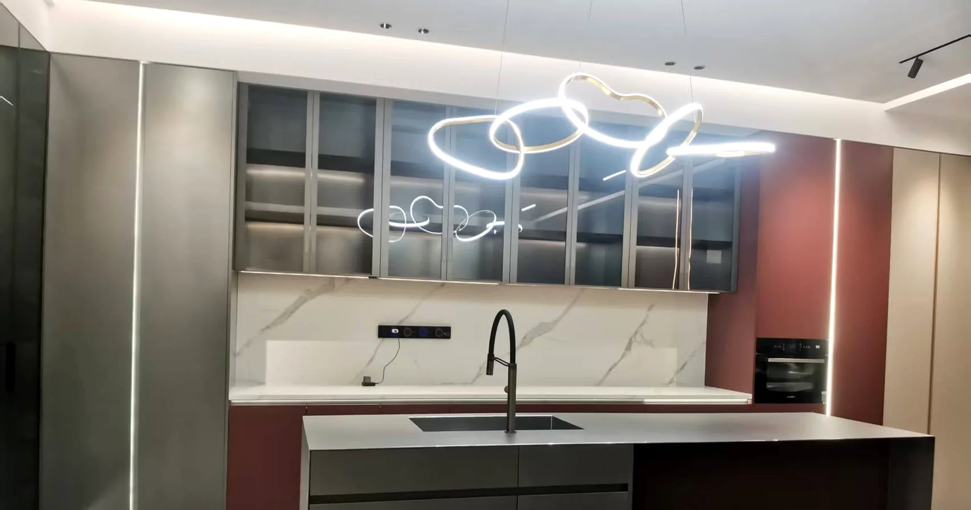 Dark flat-slab kitchen with a glass display cabinet and a marble splashback, installed for a customer.