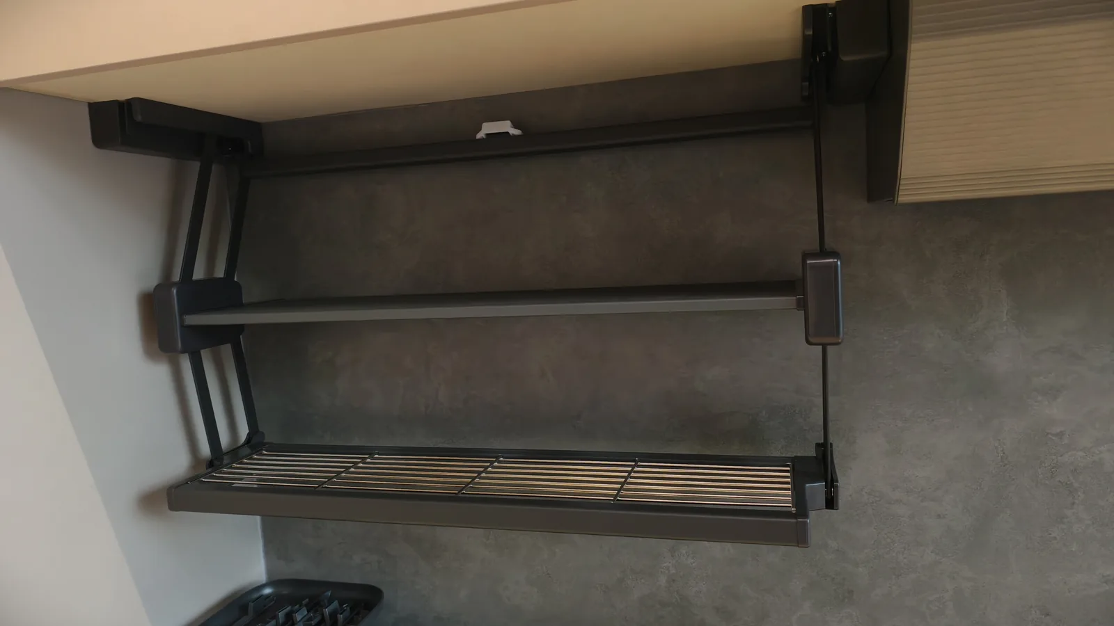 Pull-down shelf mechanism mounted inside a wall cabinet with the scissor arms extended and the wire basket shelf lowered, shot against a grey cabinet interior